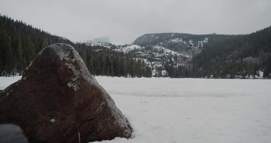 A snow covered ground with trees with a hill fog the sky and clouds in the background