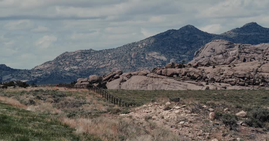 Wired fence over the rolling hills near the rock promontory close to the mountain range