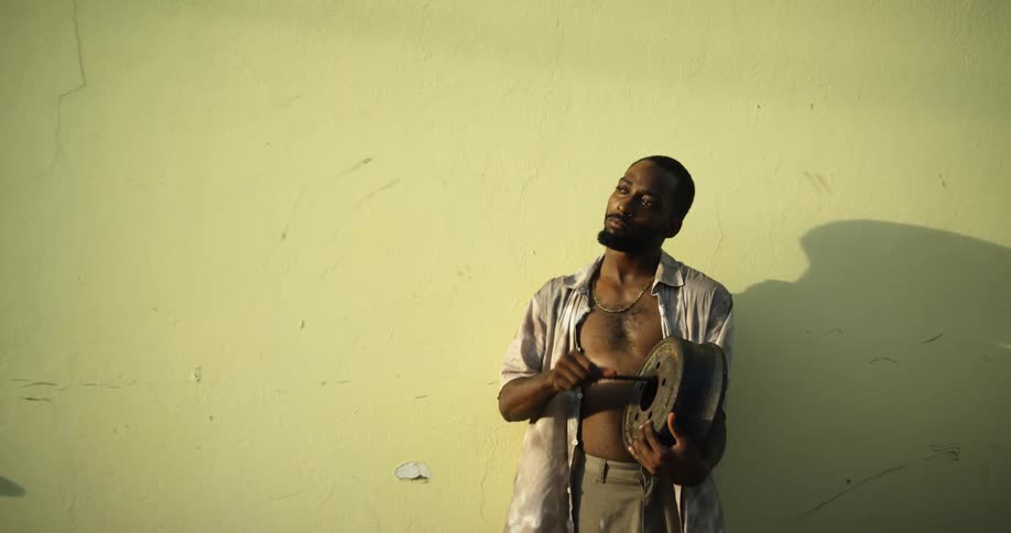 Man stands against wall casting a large shadow as he moves a bar along sides of hole in metal pan