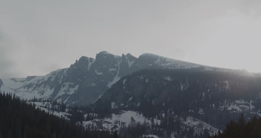 A snowy forest and mountains in the morning with fog and the sun rising from behind the mountain ridge