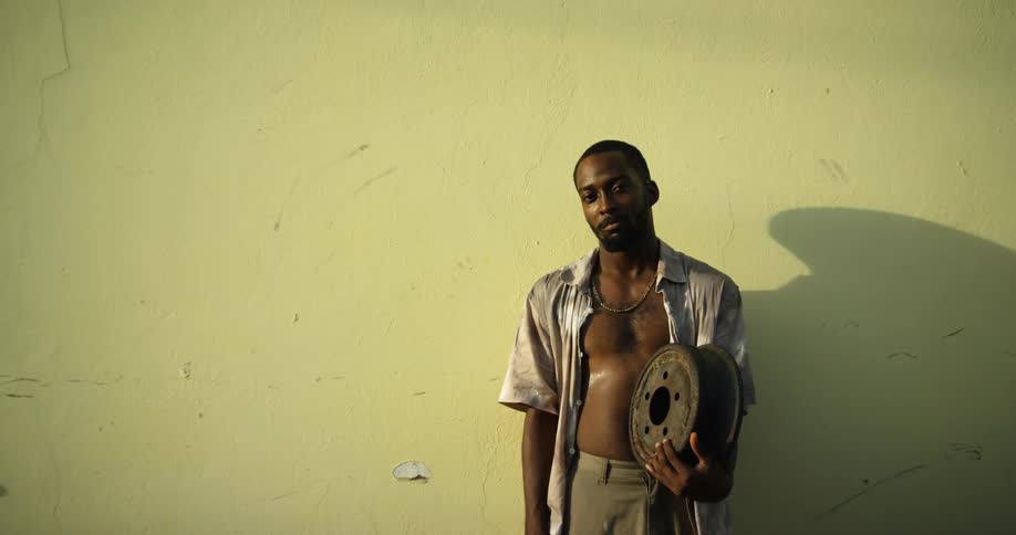 Man stands against wall casting shadow as he holds metal box and stick