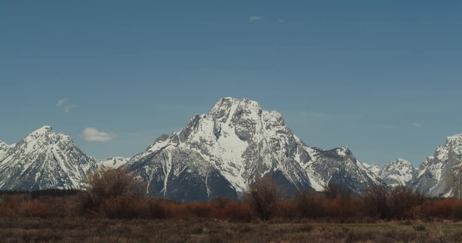 A snowy mountain range looms over a grassland on a clear day