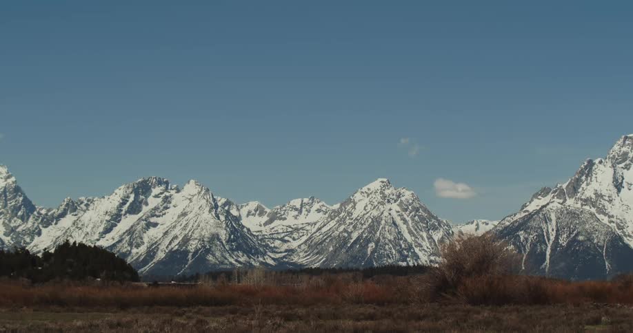 A grassy field with a snow covered mountain range with the sky and clouds in the background