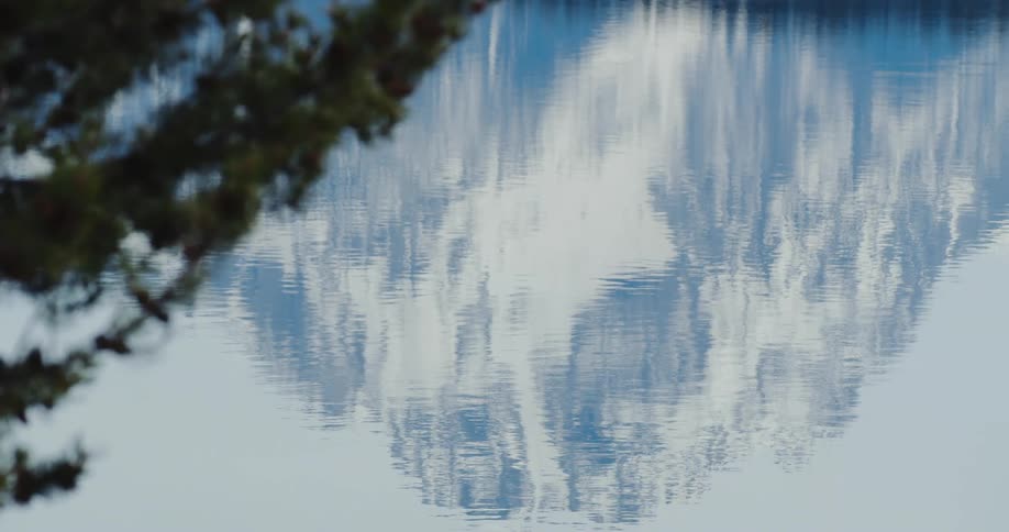 The rippling surface of a lake reflects the snow covered mountain and sky