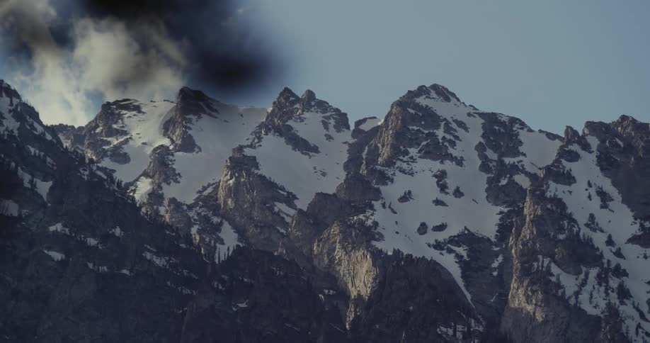 A mountain range with snow and ice with the sky and clouds in the background