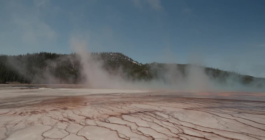Smoke moves across the dry cracked ground with mountains in the distance