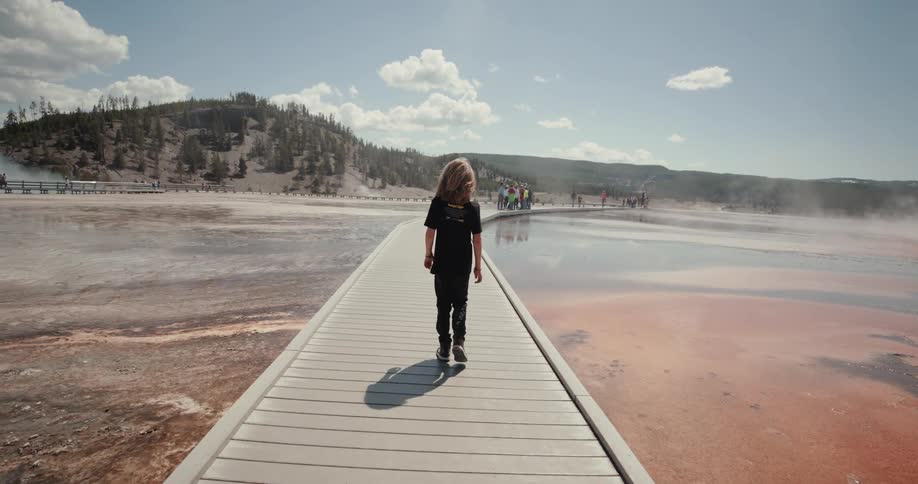 A teenager walks on the boardwalk over hot springs in a national park