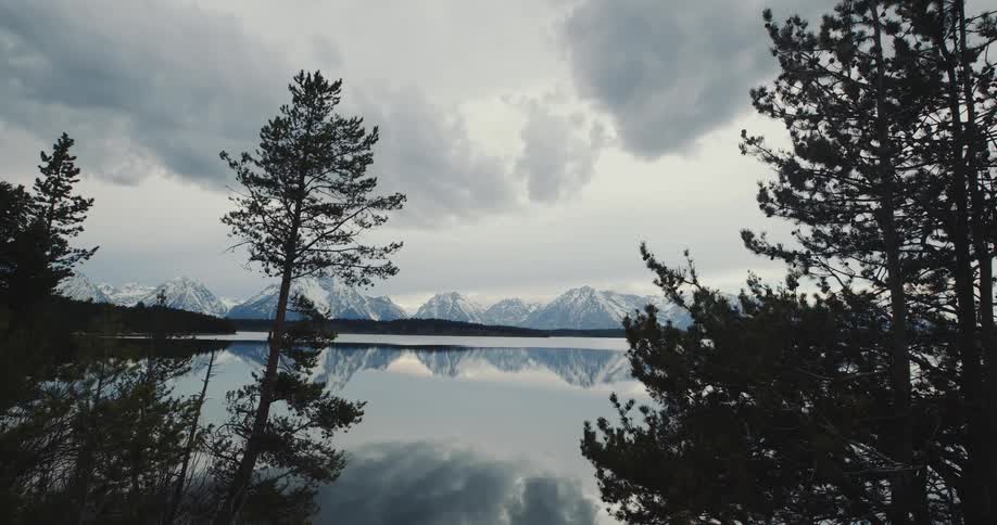 Trees and snow covered mountains reflecting on the water on a cloudy day
