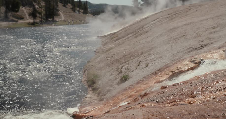 Hot springs are bubbling out of the ground and running down a slope into a river