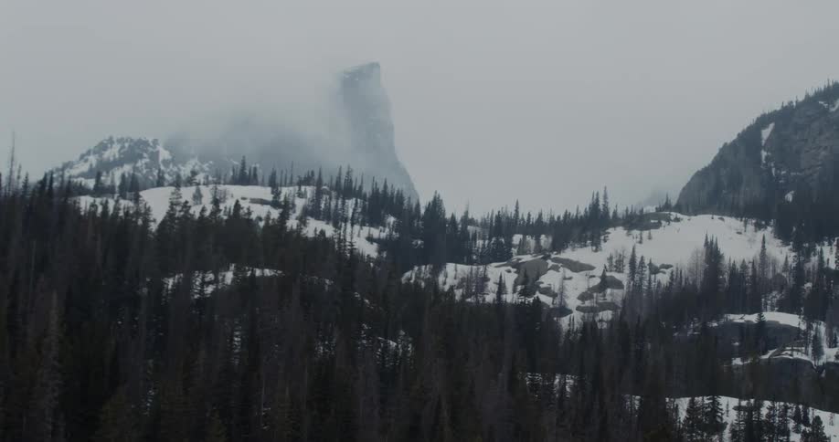A hill covered with snow and trees with a fog the sky and clouds in the background