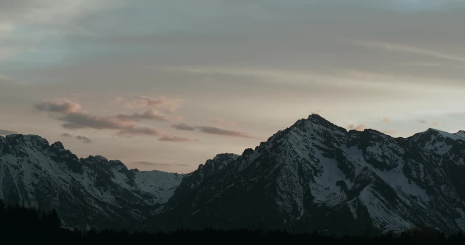A mountain range covered in snow and ice with the sky and clouds in the background