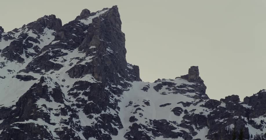 A mountain range covered in snow and ice with the sky and clouds in the background