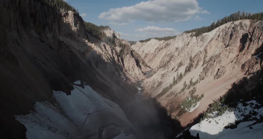 A canyon with snow patches with forest areas on the plateaus of both sides in the daytime