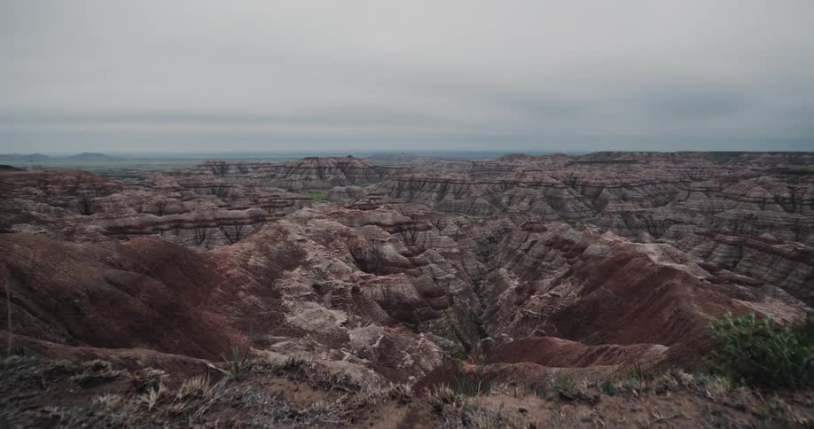 Grass tops ground overlooking badlands stretching to horizon on overcast day