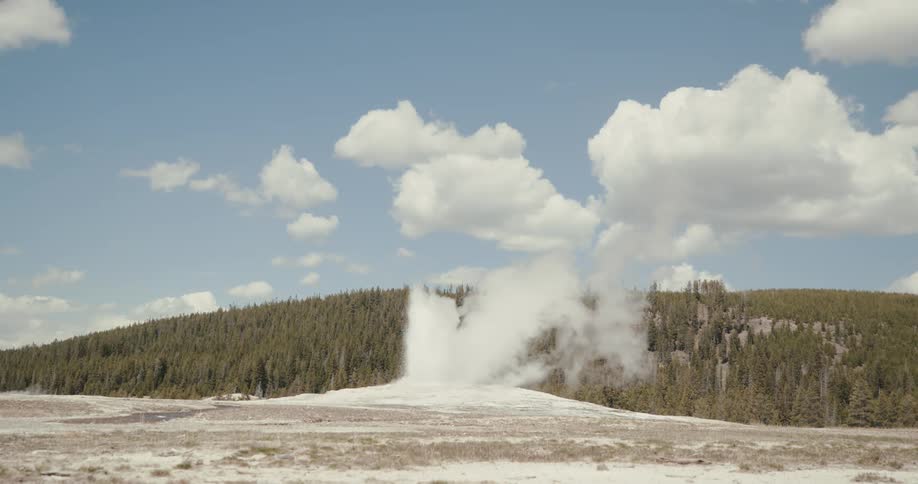 Old Faithful geyser erupts sending water straight up in the air while smoke billows