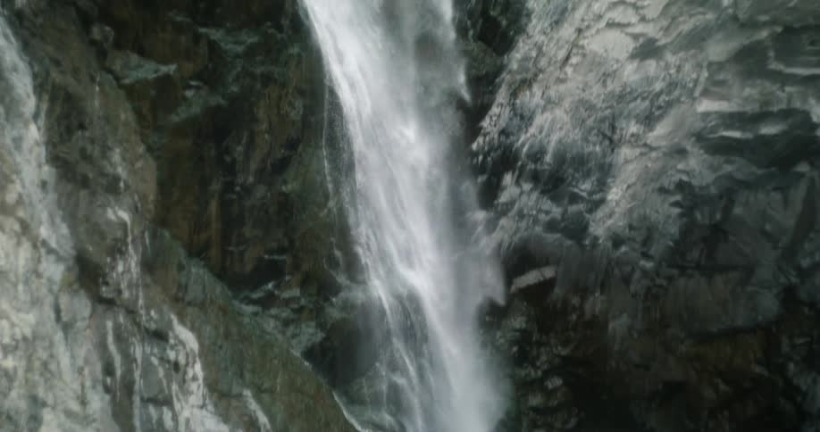 A steep waterfall plunges into a small lake at the bottom of a canyon