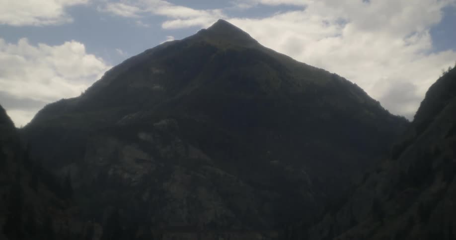 A mountain with a peak high in a cloudy sky and trees in the valley