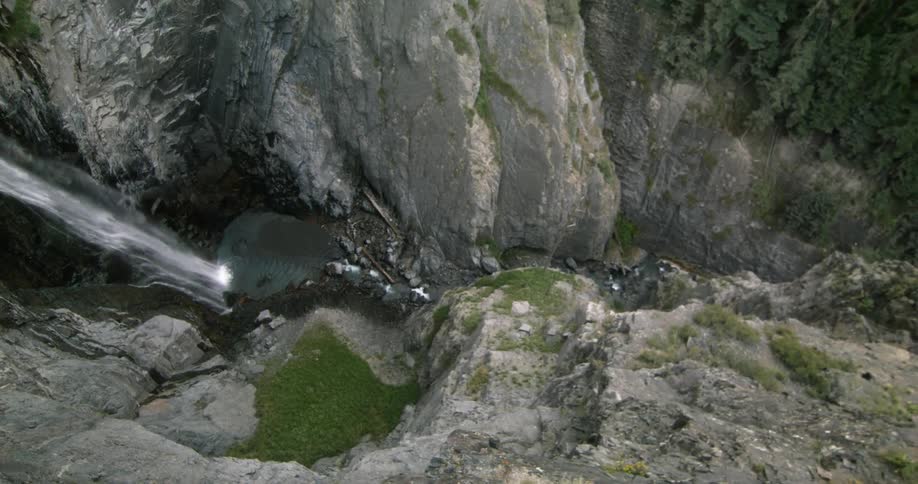 View of a canyon with evergreen trees and water falling and pooling at the bottom in the daytime