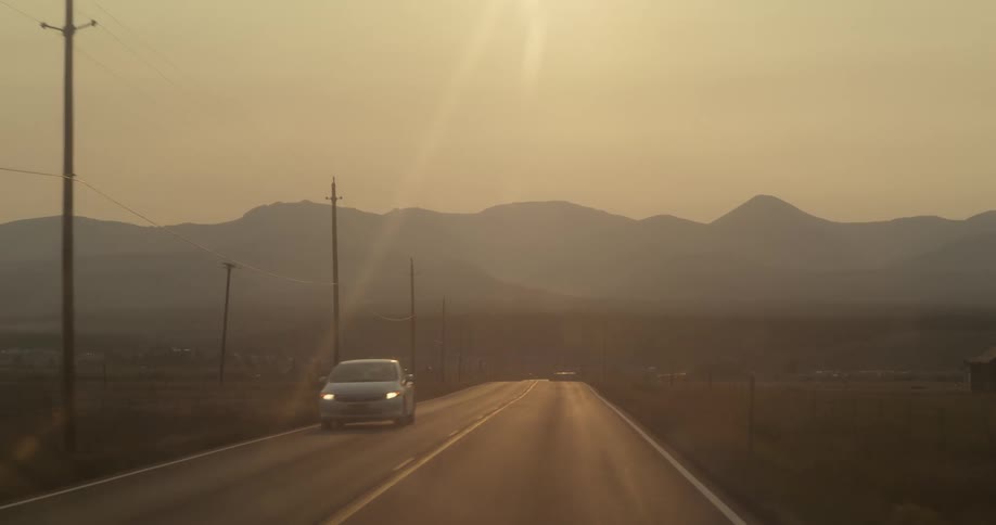 The sun shines brightly on a car traveling on a road with mountains in the distance