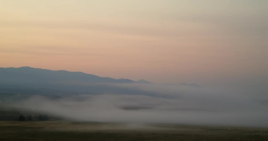 A wide shot of early morning fog over a landscape with a mountain in the background