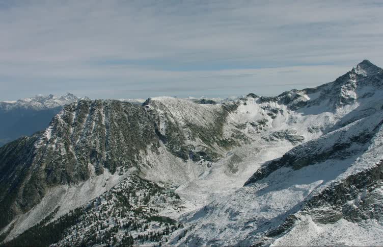 A mountain range covered in snow and ice with the sky and clouds in the background