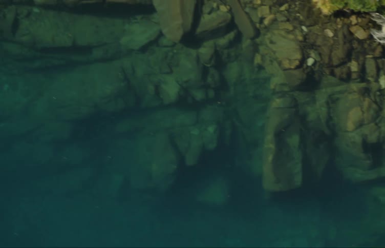 Aerial view of rocks under the green lake water near the cliffs in the mountains