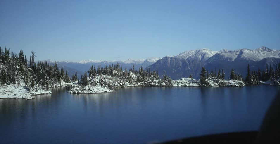 Snow covers shore forest and mountains as vehicle heads toward shore