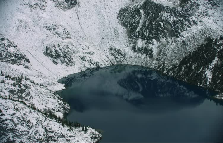 An aerial view of a lake in the winter surrounded by a snowy forested mountain during the daytime