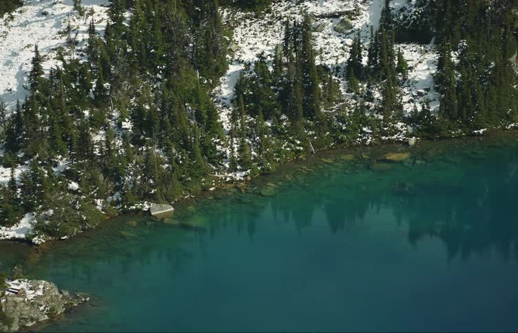 Blue water reflects conifer trees from snow covered conifer forest