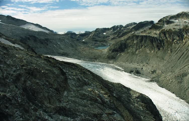 An aerial view of a glacier and surrounding rocky mountain landscape during the day