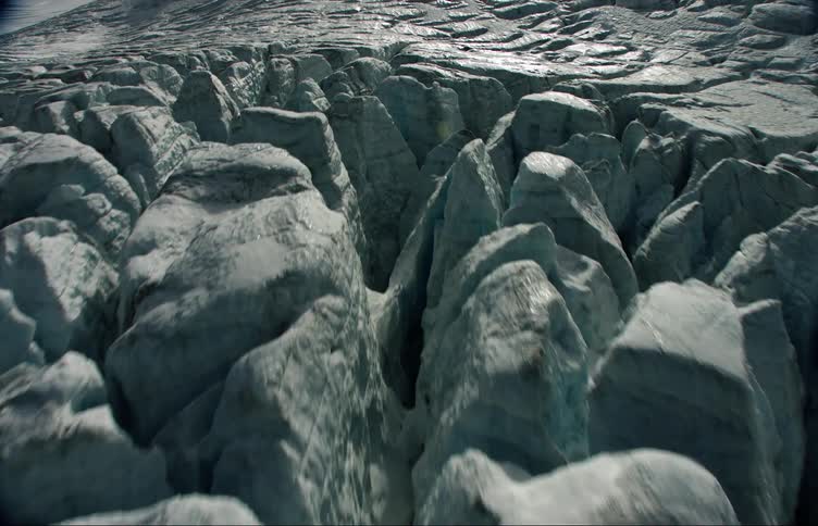 Sun shines on top of crevices on glacier bordering rock mound