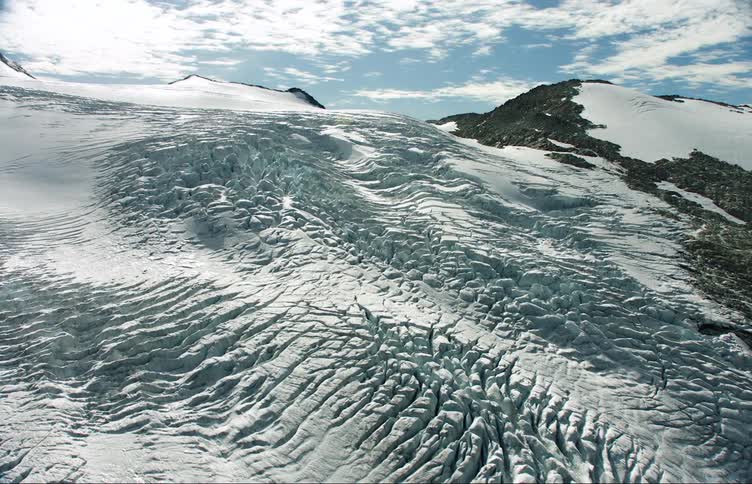 A mountain range covered in snow and ice with the sky and clouds in the background