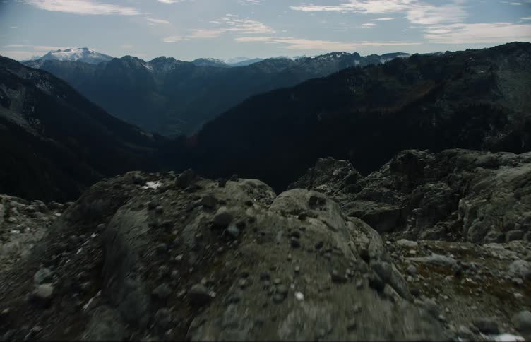 A lake surrounded by cliffs with a mountain range the sky and clouds in the background