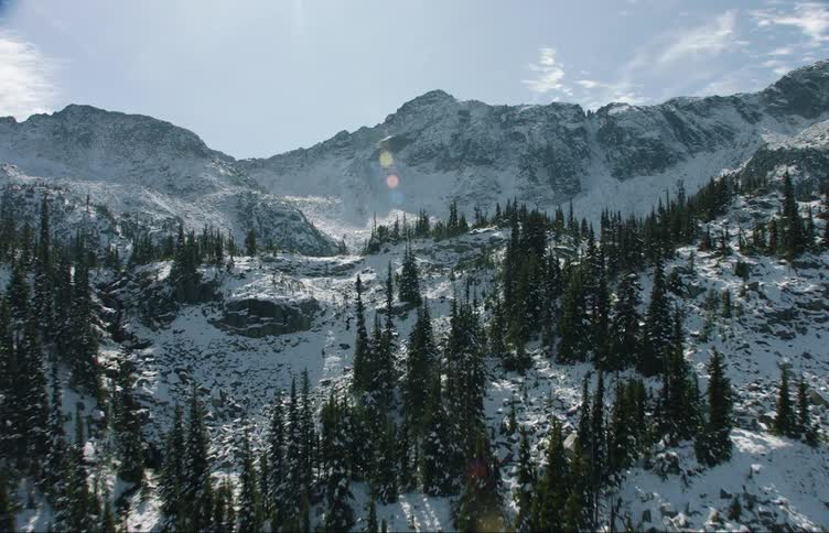 Aerial view of pine trees on the snow covered slopes of a mountain range surrounding a lake