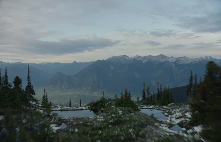 A lake with trees with a mountain range the sky and clouds in the background