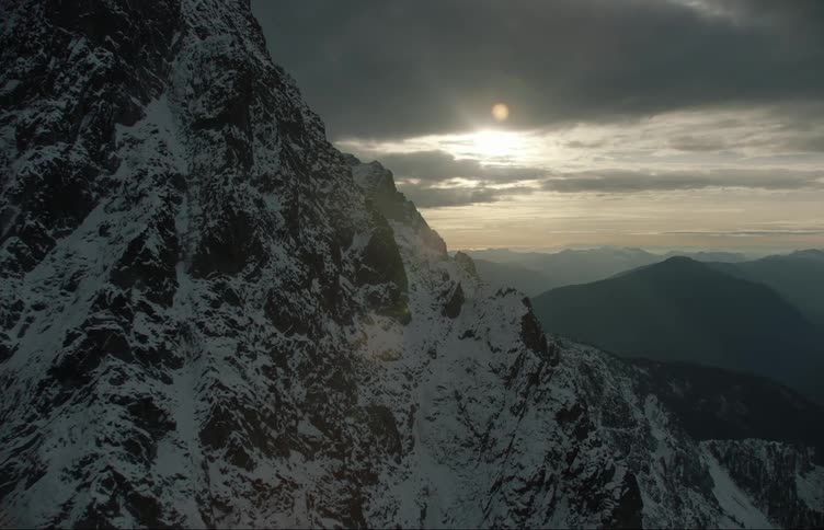 A mountain range covered in snow and ice with the sky and clouds in the background