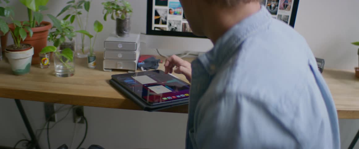 A man sitting at a table and using a camera and a tablet in front of a computer