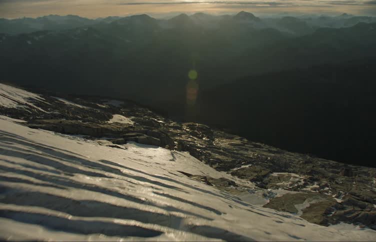 Aerial view of snow and ice covered mountain and the sun shining on the slope