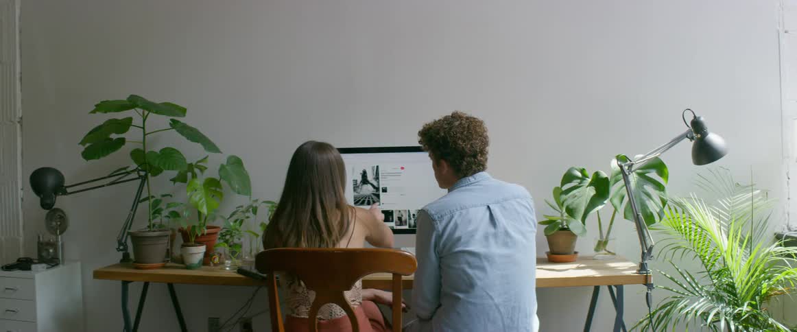 A man talks with a woman while sitting beside her at a computer desk