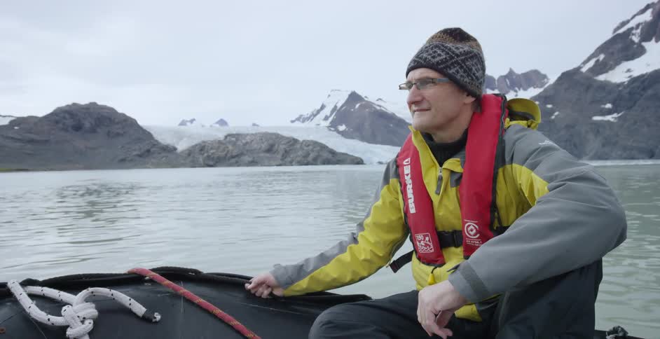 A man rides a boat near icy mountains
