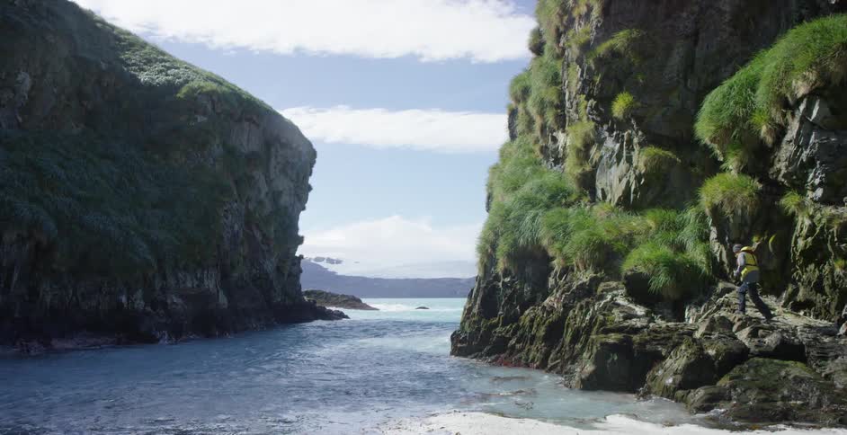 Waves crash against two cliffs as a person climbs on the side