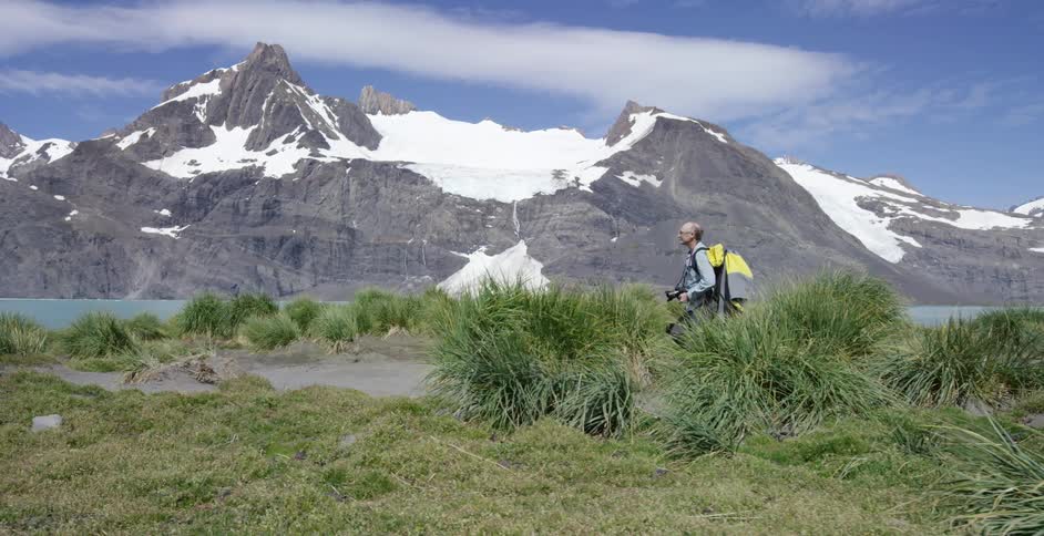 A man walks along the grass by a mountain