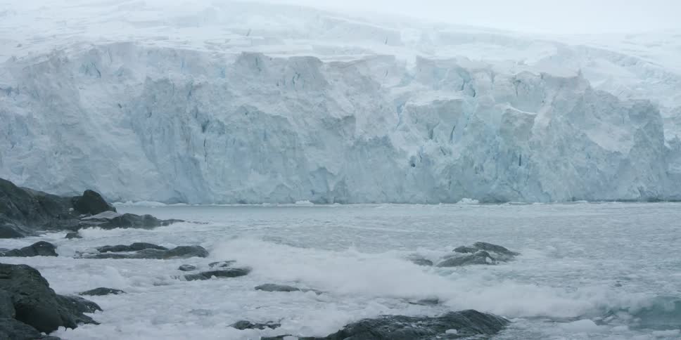 Waves crash on the rocks near an ice cliff