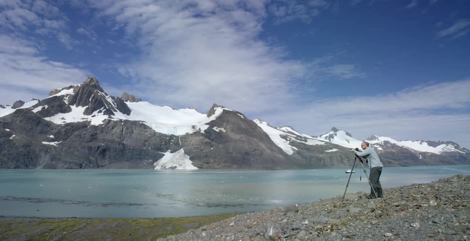 A man is photographing a mountain range by the water