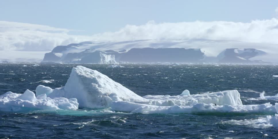 A large glacier floats on a body of water with hills in the background