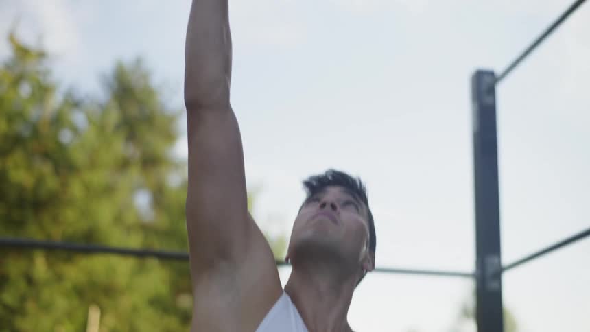 Young muscular man wearing a white undershirt working out in a park at morning