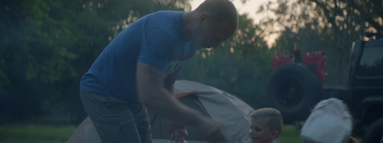 Father brings fast food to his family camping outdoors in a field at sunset