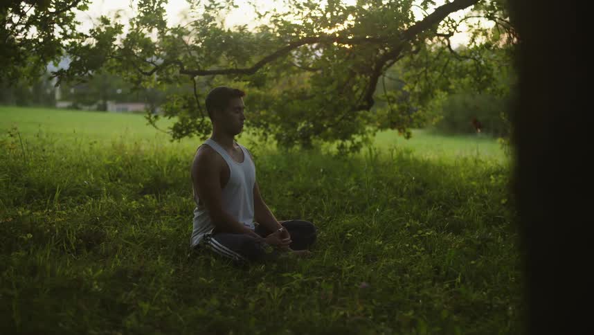 Young man meditating in a yoga position over the grass in the hill at sunset