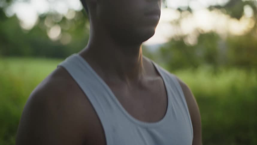 Young man wearing a white undershirt sitting on the green grass meditating at morning