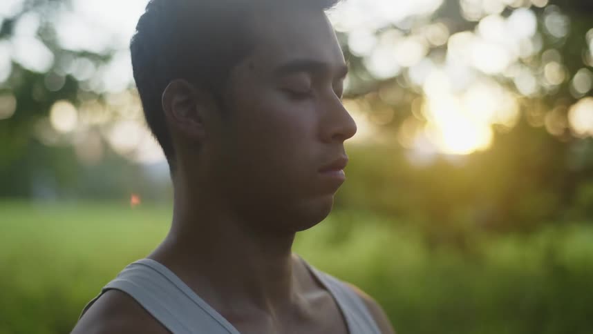 Man sits outdoors meditating with sun on horizon